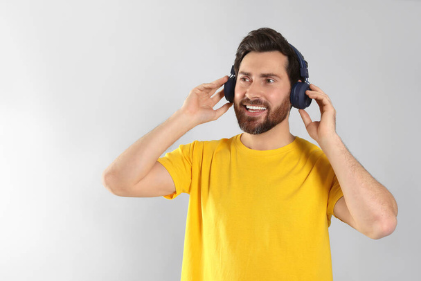 Happy man listening music with headphones on light grey background. Space for text - Fotoğraf, Görsel
