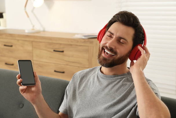 Happy man listening music with headphones on sofa indoors - Foto, imagen