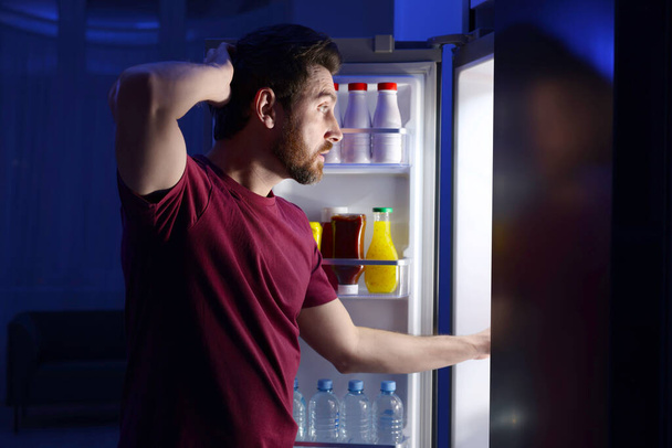 Man choosing food from refrigerator in kitchen at night. Bad habit - Zdjęcie, obraz