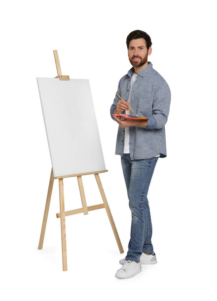 Happy man with brush and artist`s palette near easel with canvas against white background. Creative hobby - 写真・画像