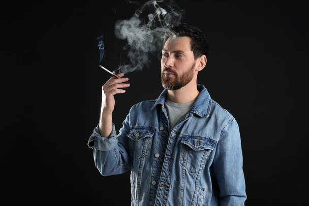 Man using cigarette holder for smoking on black background, space for text - Foto, immagini