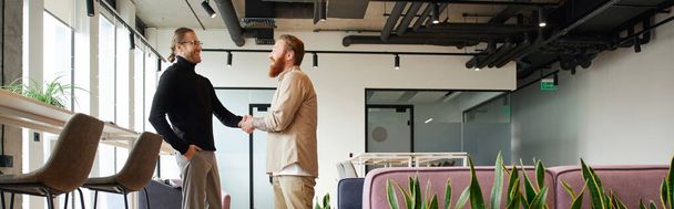 side view of entrepreneur in stylish casual clothes shaking hands with bearded and tattooed business partner and closing deal in contemporary coworking office with high tech interior, banner - Photo, Image
