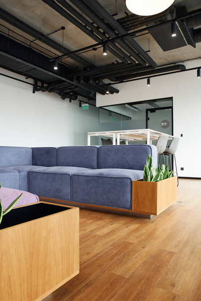 zachte en comfortabele bank in de buurt van hoge tafel en stoelen in ruime lounge van modern kantoor, coworking omgeving, high tech stijl interieur, werkruimte organisatie concept - Foto, afbeelding