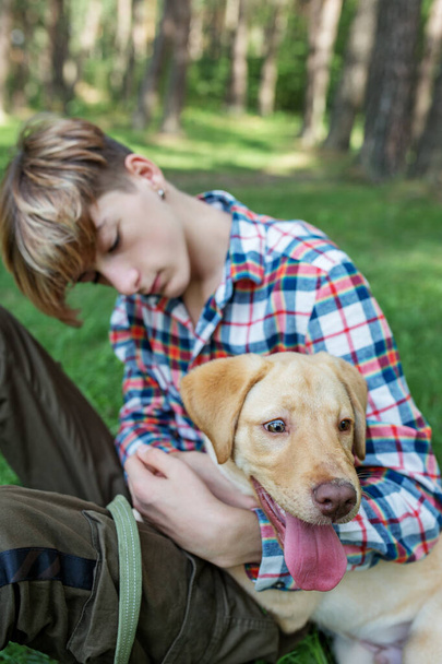 Adolescente niño abraza perro labrador en el parque en verano. Concepto de amistad y mascotas. General Z. - Foto, imagen