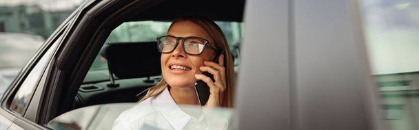 Geschäftsfrau fährt auf Rücksitz des Autos und spricht Smartphone, während sie aus dem Fenster schaut - Foto, Bild