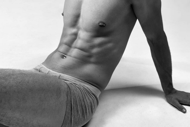 Black and white cropped image of male muscular, relief, fit, strong body. Model posing on floor in underwear. Concept of male natural beauty, body care, health, sport, fashion, ad, art - Foto, Imagem