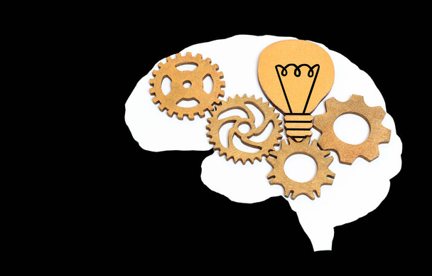 White human brain shape with wooden gears and light bulb inside isolated on black background. Creative education and enlightenment related concept. - Foto, Imagem
