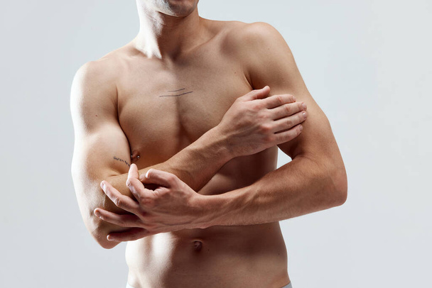 Cropped image of muscular, attractive, relief male body, breast, hands against grey studio background. SHirtless model. Concept of male natural beauty, body care, health, sport, fashion, ad - Foto, imagen
