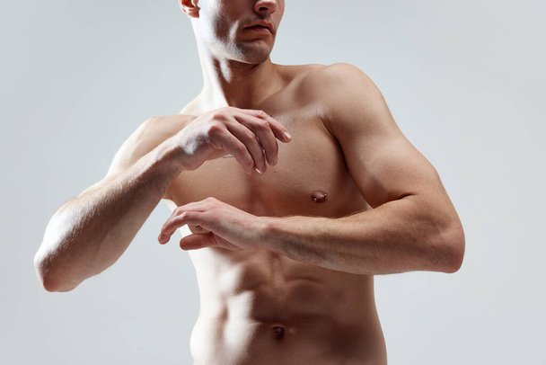 Cropped image of muscular, attractive, relief male body, breast, hands against grey studio background. SHirtless model. Concept of male natural beauty, body care, health, sport, fashion, ad - Photo, image