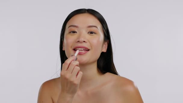 Asian woman, face and beauty, lipstick and happy in portrait, skin and makeup product on white background. Cosmetology, dermatology and skincare, mockup space and female model apply cosmetic to lips. - Footage, Video