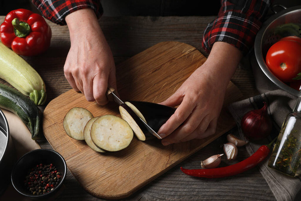 Cooking delicious ratatouille. Woman cutting fresh eggplant at wooden table, closeup - Photo, image