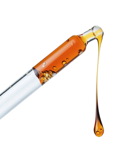 Drop of a yellow oily liquid dripping from a pipette close up isolated on a white background - Foto, immagini