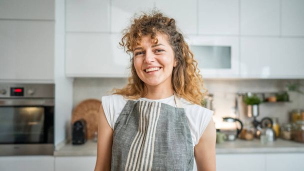 Jedna šťastná mladá dospělá běloška nosí zástěru v kuchyni úsměv - Fotografie, Obrázek