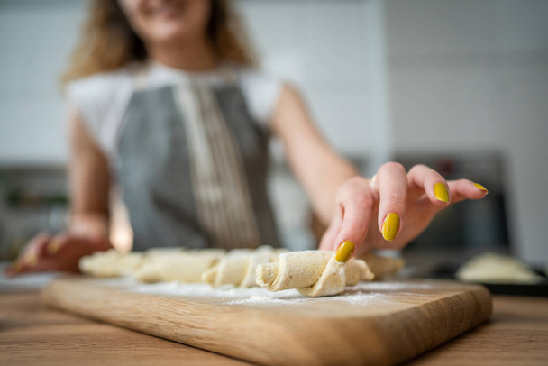 χέρια άγνωστης καυκάσιας γυναίκας φορούν ποδιά μάγειρα κρουασάν στην κουζίνα - Φωτογραφία, εικόνα