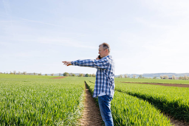 A male farmer stands in a field and talks on the phone. Modern technologies in agriculture.  - Photo, Image