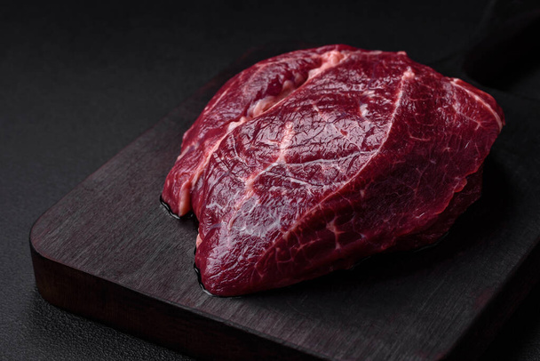 Fresh raw beef steak with salt, spices and herbs on a dark concrete background - Fotó, kép