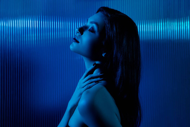 Фото юной леди в голубом ультрафиолетовом футуризме киберванна наслаждается прикосновением сауны с горячей водой на фоне неонового фильтра. - Фото, изображение