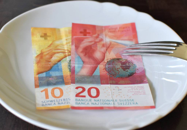 10 і 20 швейцарських франків лежать на білій тарілці з виделкою. - Фото, зображення