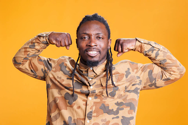 Afrikai amerikai férfi hajlító tricepsz erejét edzés előtt stúdió sárga háttér. Magabiztos sportoló személy pózol, hogy megmutassa bicepsz, izmos test fitness - Fotó, kép