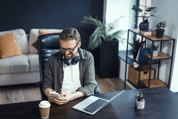 Concept of working from home, featuring mid-aged man working on laptop. Man seen in comfortable home office environment, highlighting convenience and benefits of working from comfort of ones own - Foto, afbeelding
