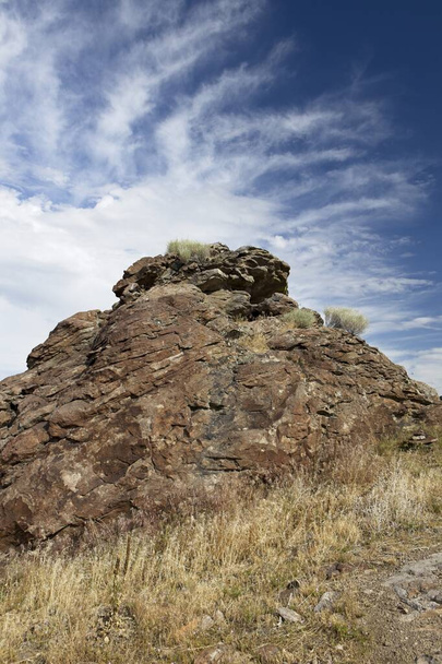 Un gran montículo de rocas sobresale de una colina situada contra un brillante cielo parcialmente nublado en el sur de Idaho. - Foto, Imagen
