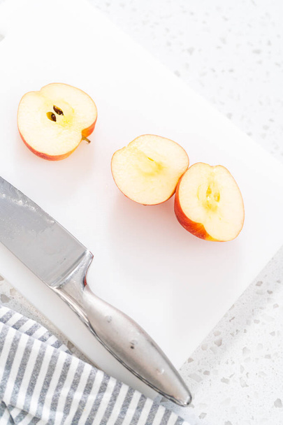 Cortar manzanas rojas en rodajas finas en una tabla de cortar blanca. - Foto, imagen