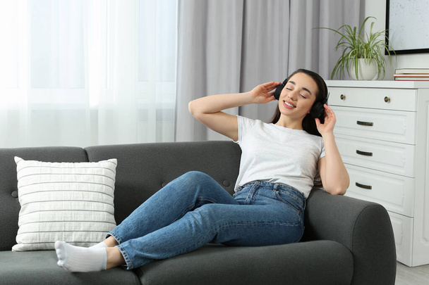 Happy woman in headphones enjoying music on soft sofa at home - Photo, Image
