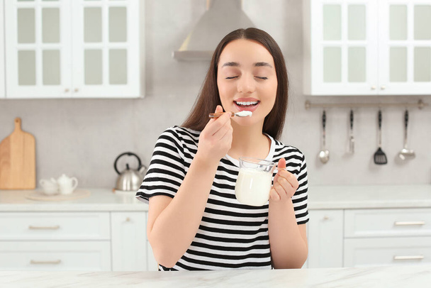 Happy woman eating tasty yogurt in kitchen - Photo, Image