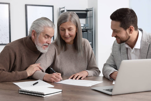 Elderly couple consulting insurance agent about pension plan at wooden table indoors - Foto, Imagen