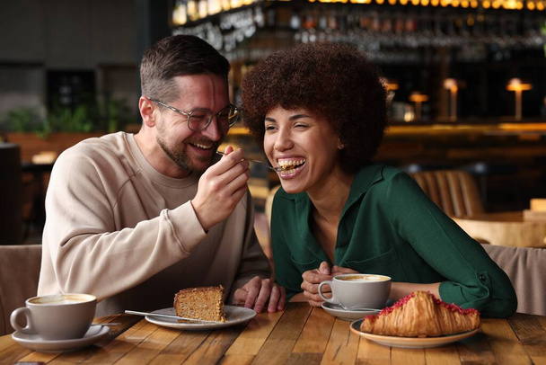 International dating. Handsome man feeding his girlfriend with cake in cafe - Foto, afbeelding