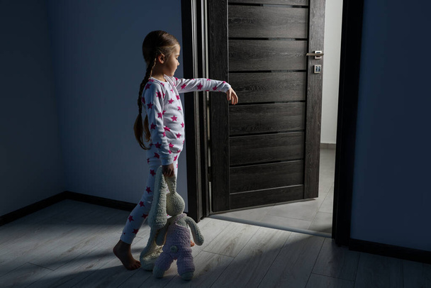 Girl in pajamas with toy bunny sleepwalking indoors at night - Foto, afbeelding