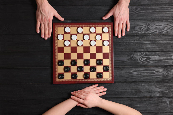 Man playing checkers with woman at black wooden table, top view - Photo, image