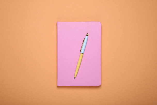 Closed pink office notebook on pale orange background, top view - Fotografie, Obrázek