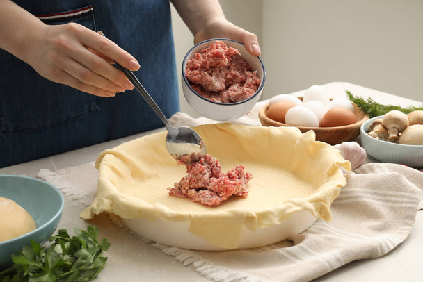 Woman putting meat into baking dish with dough to make pie at light grey table, closeup - Foto, imagen