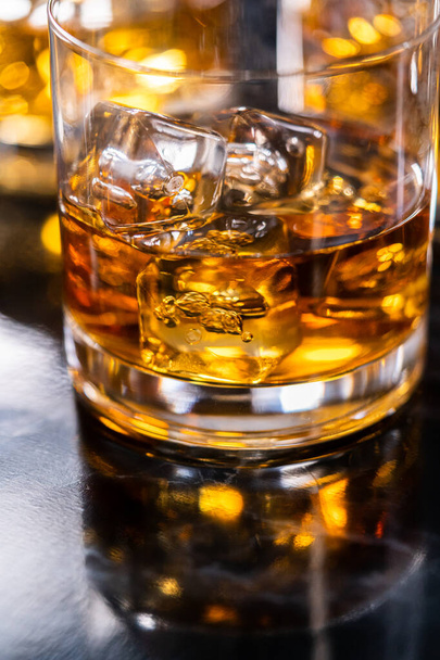 Scotch on the rocks in whiskey glass on a black marble surface. - Фото, изображение