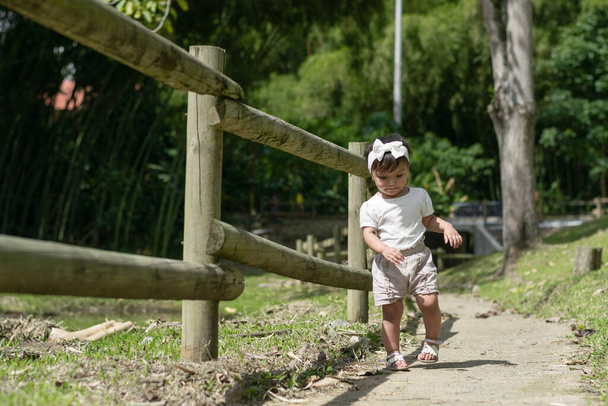 little brunette latina girl learning to walk along a path in a park - Foto, afbeelding