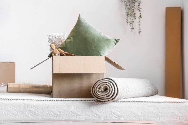 Bed with cardboard box and rolled carpet in room on moving day - Foto, Imagen