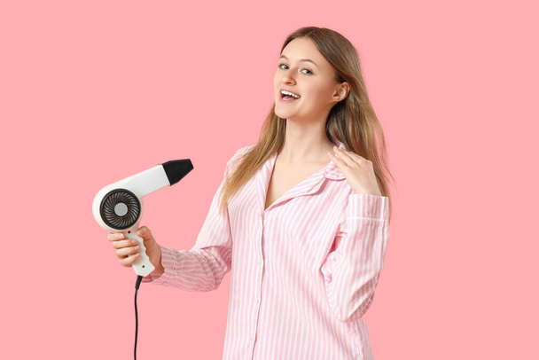 Beautiful young woman with hair dryer on pink background - 写真・画像