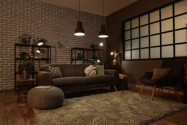 Interior of dark living room with cozy grey sofa and glowing lamps - Foto, Imagen