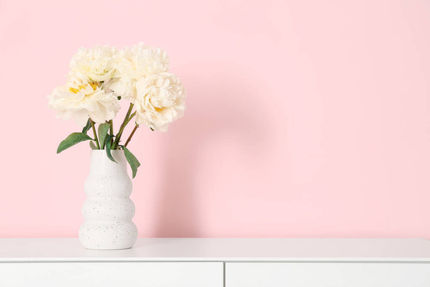 Váza fehér bazsarózsa a komód közelében rózsaszín fal - Fotó, kép