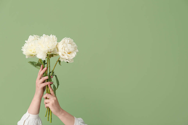 Vrouwelijke handen met witte pioenrozen op groene achtergrond - Foto, afbeelding