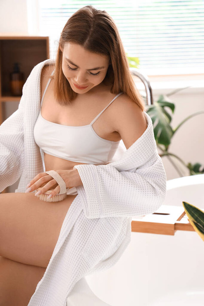 Jeune femme massant sa jambe avec une brosse anti-cellulite dans la salle de bain - Photo, image