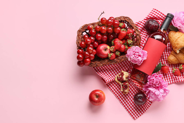 Összetétel ízletes ételekkel piknikezéshez, borosüveggel és bazsarózsa virágokkal rózsaszín alapon - Fotó, kép