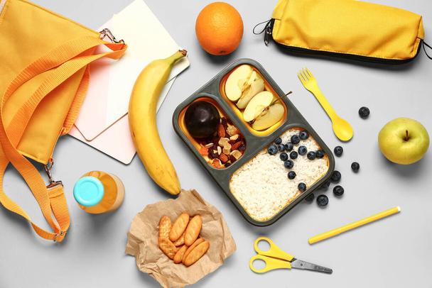 Рюкзак, канцелярські товари та обідня коробка зі смачною їжею на сірому фоні - Фото, зображення