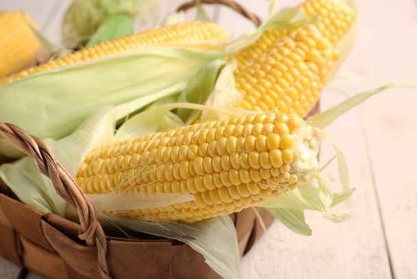 Wicker basket with fresh corn cobs on white wooden background, closeup - Zdjęcie, obraz