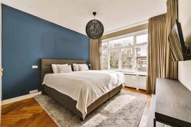 une chambre avec parquet et mur d'accentuation bleu derrière le lit est une grande fenêtre qui donne sur la rue - Photo, image