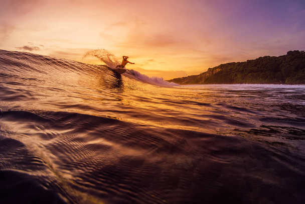 14 de diciembre de 2022. Bali, Indonesia. Hombre en el océano tropical durante el surf con tonos de atardecer o amanecer. Surfista paseo en ola y hacer trucos. - Foto, imagen
