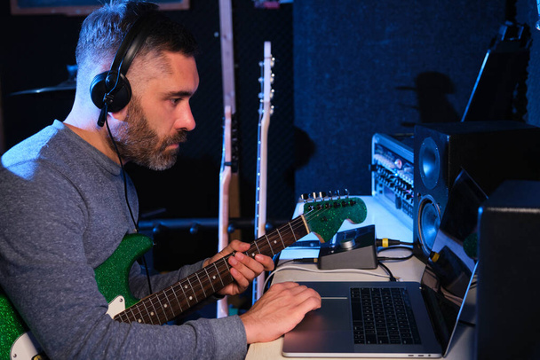 Muzyk dostosowujący dźwięk swojej gitary elektrycznej do słuchawek i laptopa w studiu nagraniowym. Produkcja muzyczna. - Zdjęcie, obraz