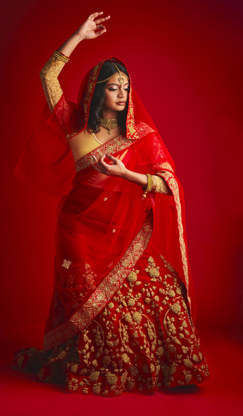 Μόδα, χορός και Ινδή γυναίκα σε ένα παραδοσιακό φόρεμα, γιορτή και αυτοπεποίθηση σε ένα κόκκινο φόντο στούντιο. Γυναίκα, κορίτσι και μοντέλο με πολιτιστικό ντύσιμο, χορεύτρια και τελετουργικό με αυτοπεποίθηση. - Φωτογραφία, εικόνα