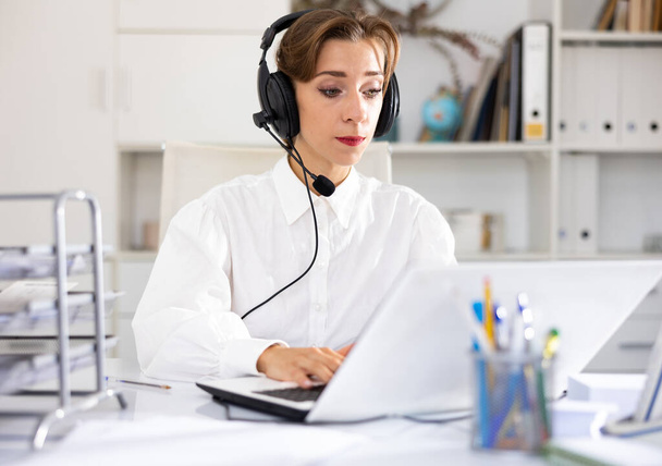 Attractive young woman using headphones with microphone and laptop while working in call center. - Foto, Imagen
